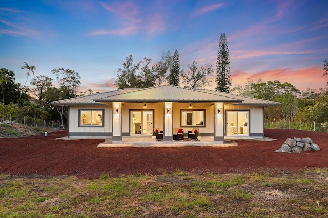 back of house at dusk featuring board and batten siding, metal roof, and a patio