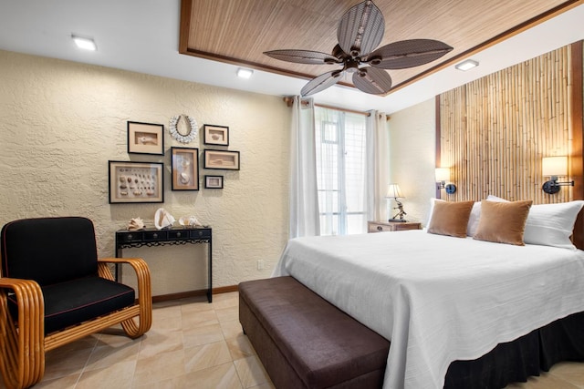 bedroom featuring baseboards, a raised ceiling, ceiling fan, and a textured wall