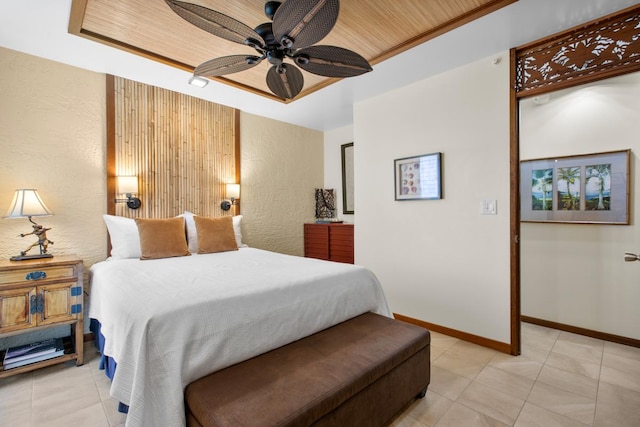 bedroom featuring light tile patterned floors, baseboards, a tray ceiling, and ceiling fan
