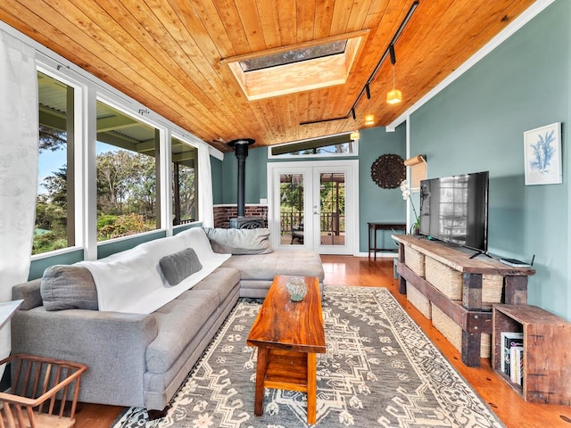 living area with rail lighting, wood ceiling, a wood stove, a skylight, and wood finished floors