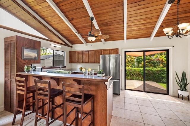 kitchen featuring brown cabinetry, freestanding refrigerator, a peninsula, wooden ceiling, and light tile patterned floors