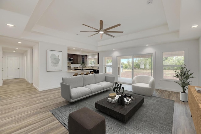living area featuring ceiling fan, a raised ceiling, light wood-style floors, recessed lighting, and baseboards