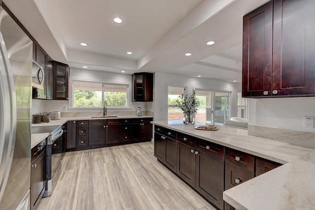 kitchen featuring glass insert cabinets, a tray ceiling, a sink, light wood-style flooring, and appliances with stainless steel finishes