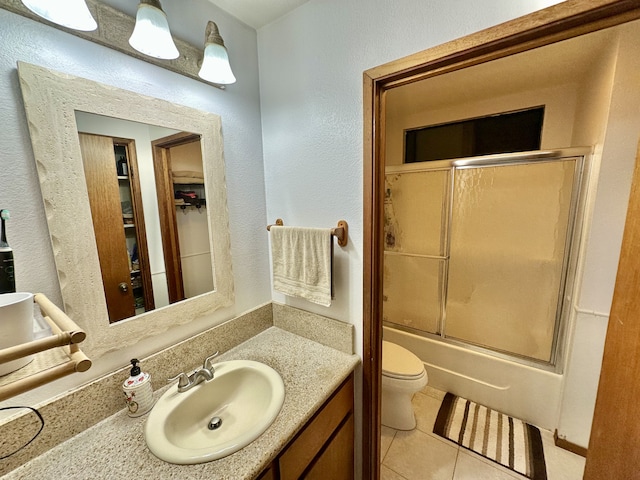 full bath featuring tile patterned floors, vanity, toilet, shower / bath combination with glass door, and a textured wall