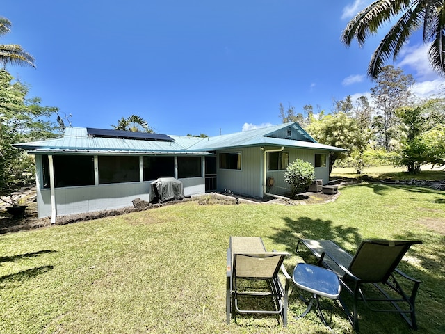 back of property featuring a sunroom, roof mounted solar panels, a lawn, and metal roof