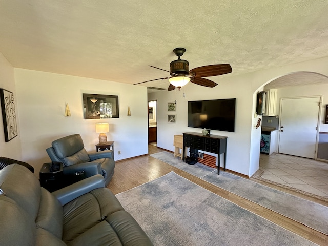 living area with arched walkways, ceiling fan, baseboards, a textured ceiling, and wood finished floors