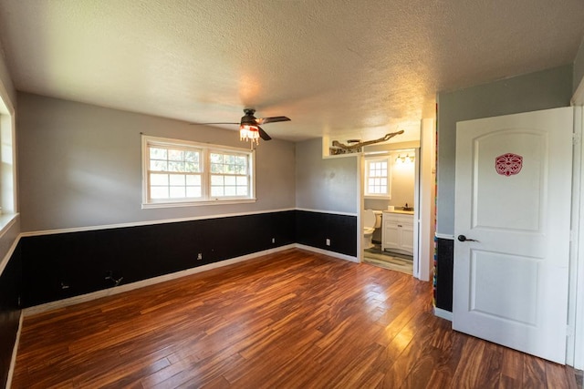 spare room with a textured ceiling, baseboards, a ceiling fan, and dark wood finished floors