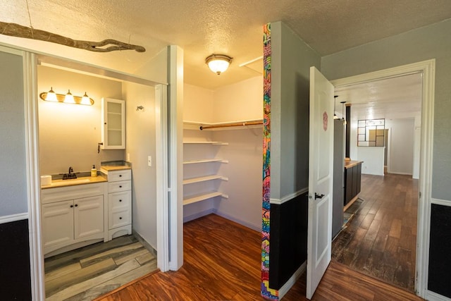 interior space featuring vanity, a textured ceiling, a walk in closet, and wood finished floors