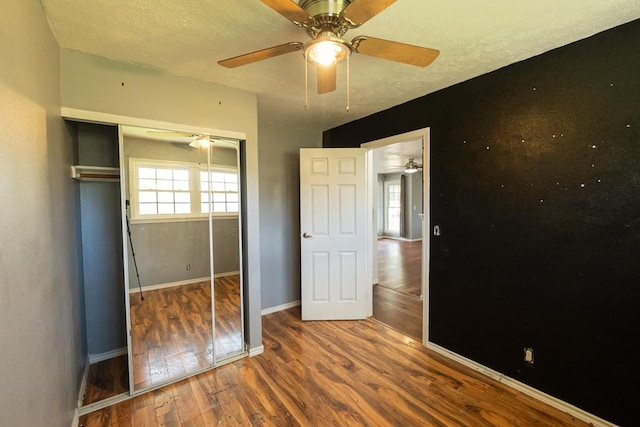 unfurnished bedroom featuring a ceiling fan, a closet, a textured ceiling, baseboards, and wood finished floors