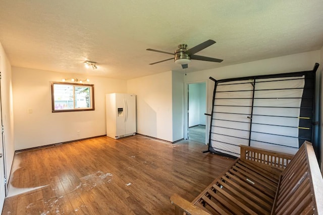 unfurnished living room with ceiling fan, hardwood / wood-style flooring, a textured ceiling, and baseboards