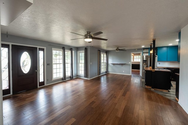 unfurnished living room featuring baseboards, dark wood-style flooring, ceiling fan, and a textured ceiling