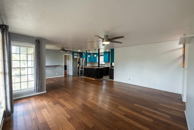 unfurnished living room with a textured ceiling, baseboards, a ceiling fan, and dark wood-type flooring
