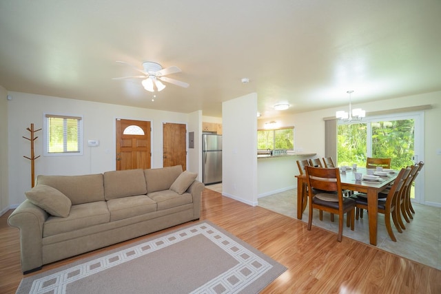 living room featuring light wood-type flooring, a chandelier, baseboards, and ceiling fan