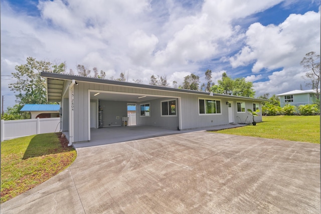 exterior space with concrete driveway, fence, a lawn, and a carport