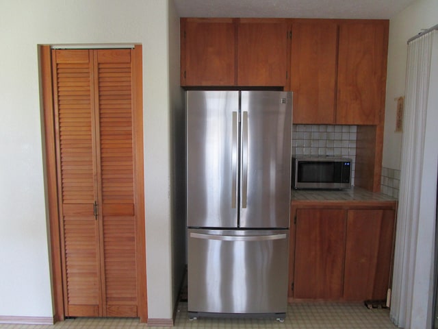 kitchen with appliances with stainless steel finishes, tile counters, brown cabinets, and decorative backsplash