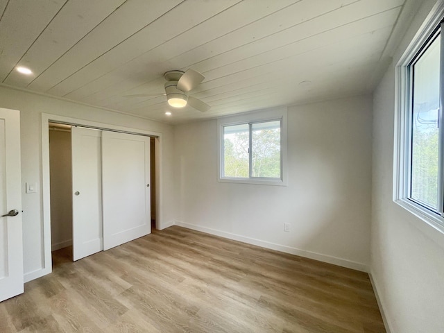 unfurnished bedroom featuring light wood-type flooring, baseboards, a closet, and multiple windows