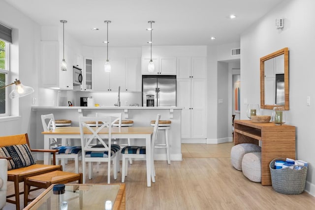kitchen with visible vents, a peninsula, glass insert cabinets, light wood-style floors, and stainless steel fridge with ice dispenser