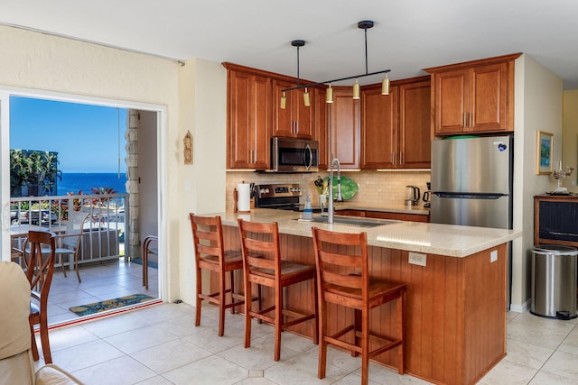 kitchen with a peninsula, brown cabinets, tasteful backsplash, a sink, and appliances with stainless steel finishes
