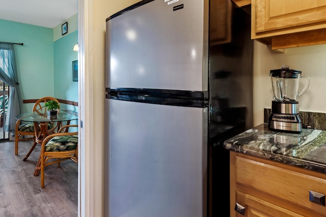 kitchen featuring freestanding refrigerator, wood finished floors, dark stone countertops, and light brown cabinets