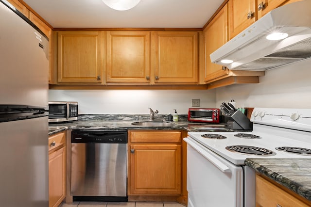 kitchen featuring appliances with stainless steel finishes, under cabinet range hood, a sink, light tile patterned floors, and dark stone countertops