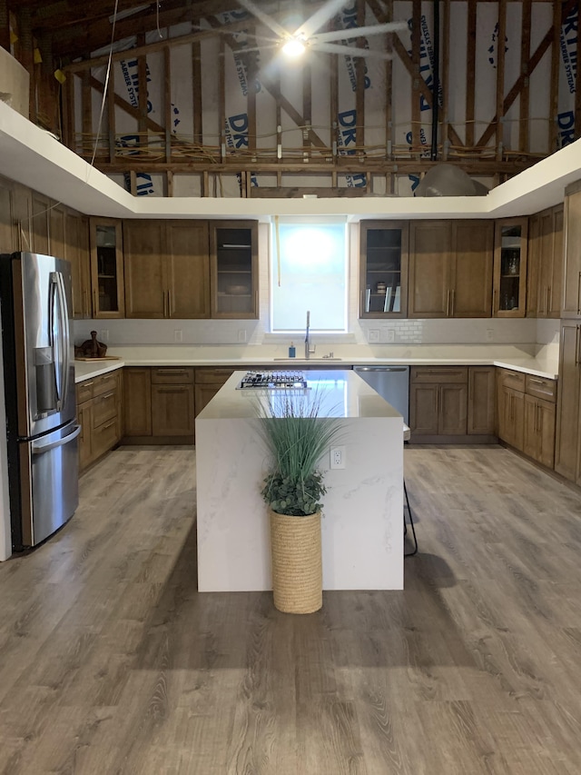 kitchen featuring brown cabinetry, a towering ceiling, glass insert cabinets, a sink, and stainless steel appliances