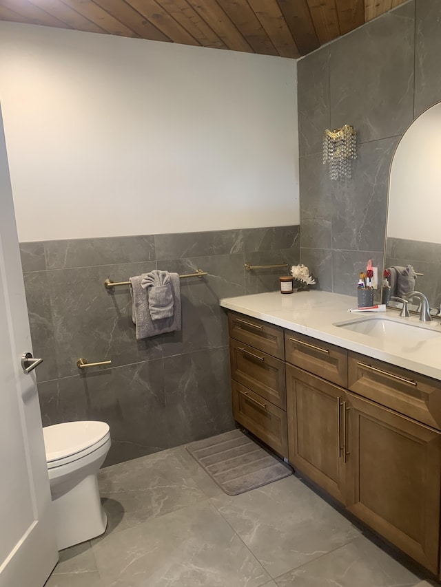 bathroom with vanity, toilet, wooden ceiling, and tile walls