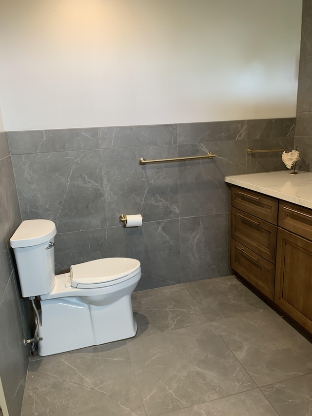 half bathroom with toilet, tile walls, a wainscoted wall, and vanity