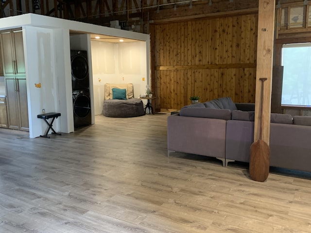 living area with wooden walls, stacked washer and dryer, a high ceiling, and wood finished floors