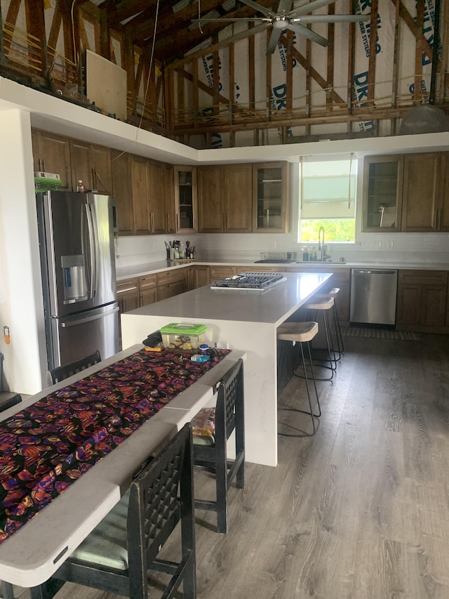 kitchen featuring brown cabinetry, a breakfast bar area, appliances with stainless steel finishes, wood finished floors, and high vaulted ceiling