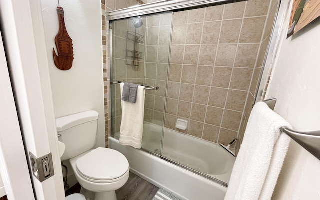 bathroom featuring toilet, wood finished floors, and bath / shower combo with glass door