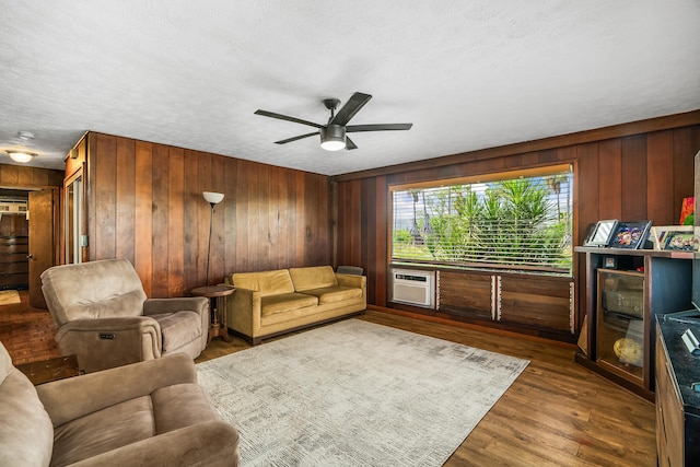 living room with wood walls, ceiling fan, wood finished floors, and a wall unit AC