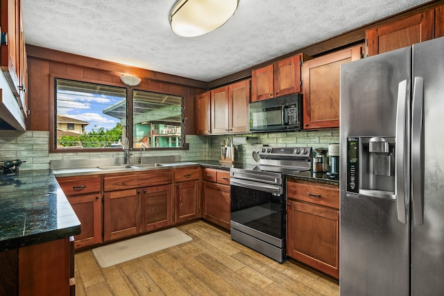 kitchen featuring a sink, a textured ceiling, stainless steel appliances, decorative backsplash, and light wood-type flooring