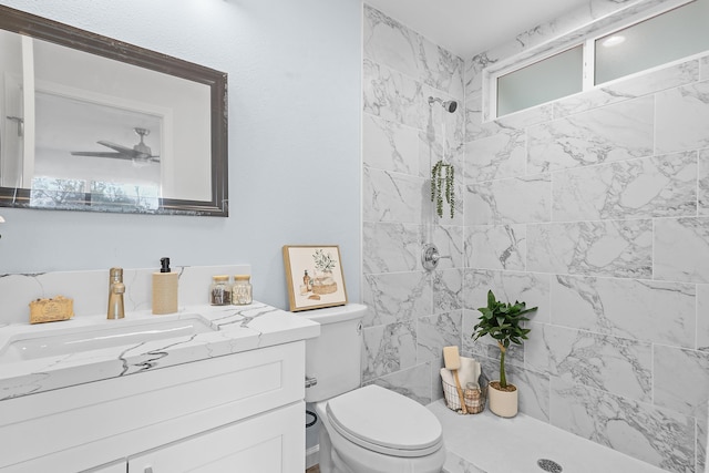 bathroom featuring tiled shower, toilet, vanity, and ceiling fan