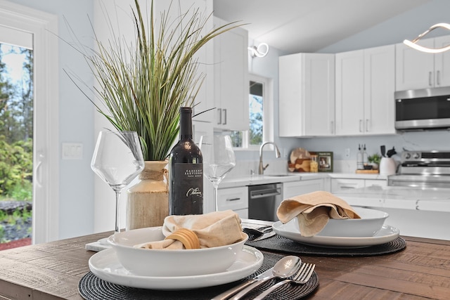 kitchen featuring appliances with stainless steel finishes, white cabinets, lofted ceiling, a sink, and wood finished floors