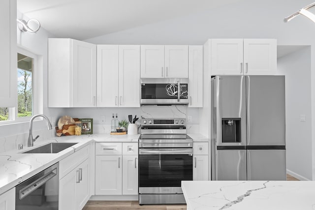 kitchen featuring stainless steel appliances, a sink, vaulted ceiling, white cabinets, and light stone counters