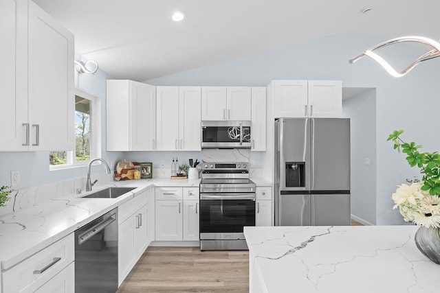 kitchen with stainless steel appliances, a sink, lofted ceiling, light wood-style flooring, and white cabinets