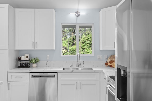 kitchen featuring appliances with stainless steel finishes, a sink, white cabinets, and light stone counters