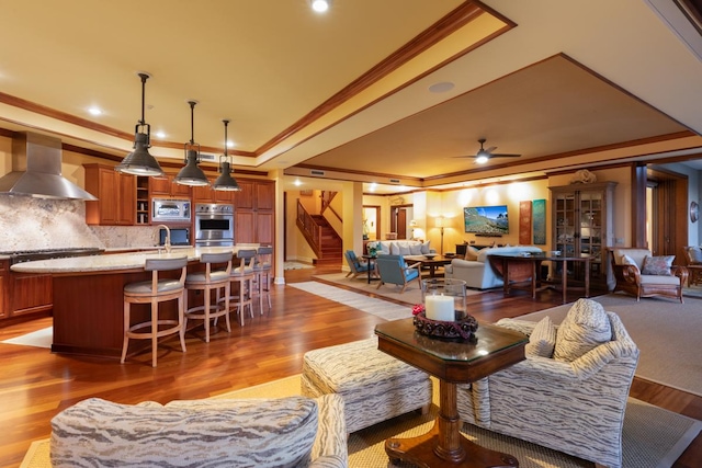 living room featuring ornamental molding, stairway, wood finished floors, ceiling fan, and a raised ceiling