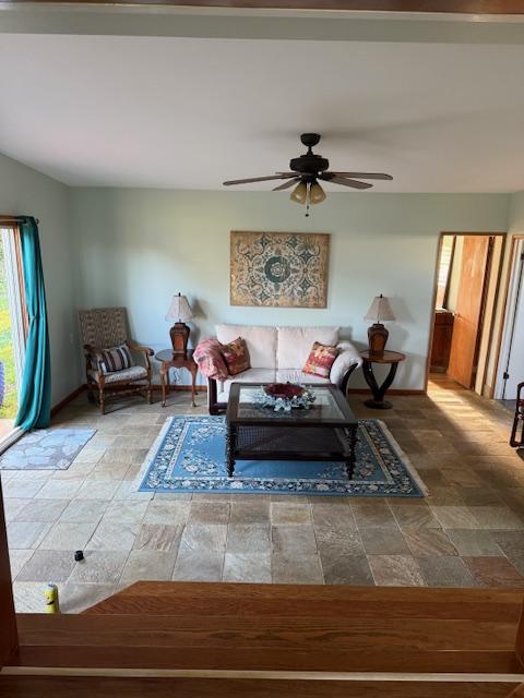 living area featuring baseboards, ceiling fan, and stone finish floor