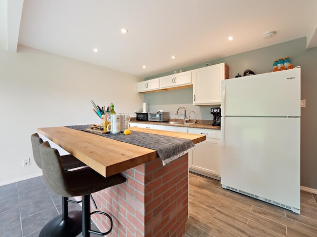 kitchen with freestanding refrigerator, a sink, a kitchen island, and white cabinets