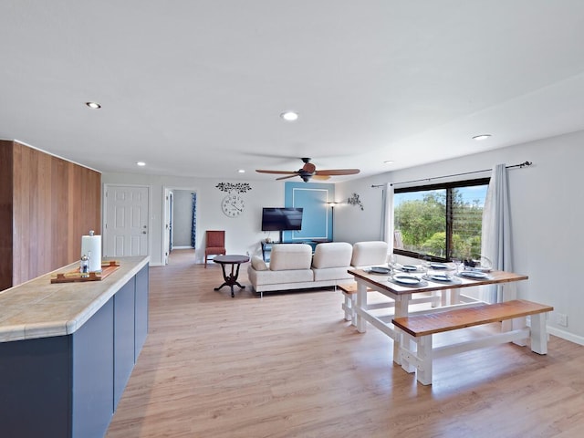living room with ceiling fan, light wood finished floors, wood walls, recessed lighting, and baseboards
