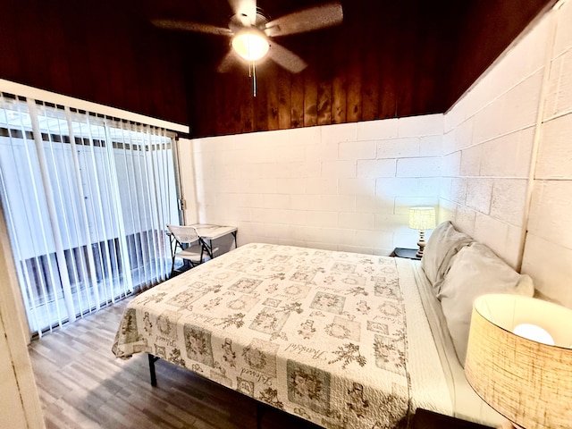 bedroom with concrete block wall, wood finished floors, and ceiling fan