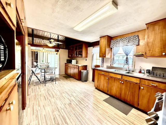 kitchen featuring a sink, brown cabinetry, ceiling fan, black microwave, and light countertops