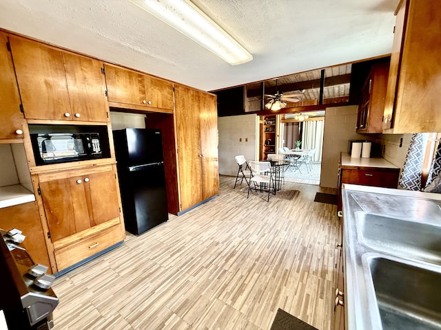 kitchen featuring ceiling fan, a sink, brown cabinets, black appliances, and light wood-style floors
