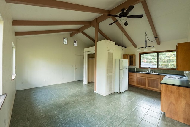 kitchen featuring brown cabinetry, lofted ceiling with beams, freestanding refrigerator, a ceiling fan, and dark countertops