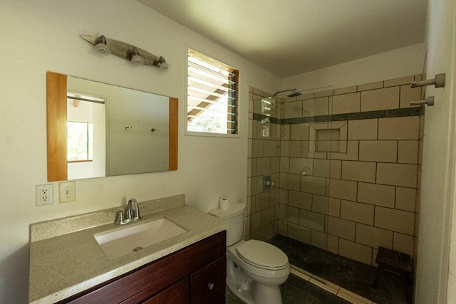 bathroom featuring toilet, tiled shower, and vanity