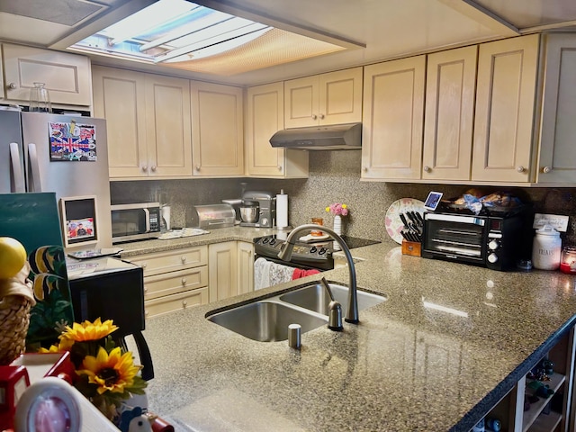 kitchen featuring stainless steel microwave, under cabinet range hood, a sink, tasteful backsplash, and light stone countertops
