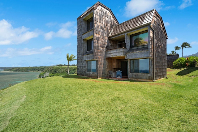 back of house with a balcony, a water view, and a lawn