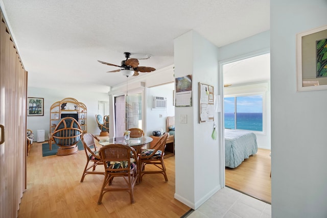 dining area with a textured ceiling, light wood-type flooring, baseboards, ceiling fan, and an AC wall unit