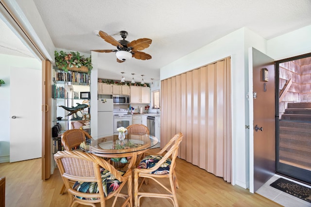 dining room with vaulted ceiling, light wood-style flooring, a textured ceiling, and a ceiling fan
